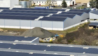 Aerial view of solar power plant with blue photovoltaic panels mounted on industrial building roof for producing green ecological electricity. Production of sustainable energy concept.